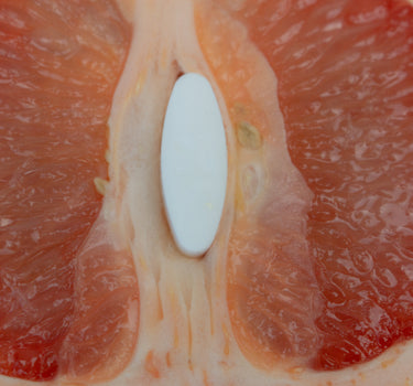 A half of grapefruit cut in half, laying flat and open with a Boquet white oval suppositories in the middle, like a metaphor for female genitals.