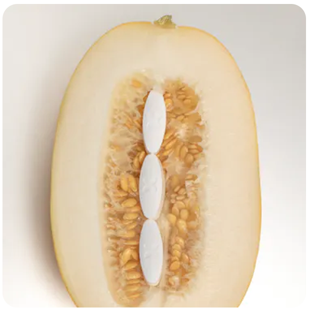 A melon cut in half with 3 Boquet oval white pills in the centre, a metaphor for female genitals
